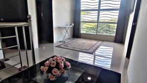 A modern living room with a glass coffee table, a TV, and a large window with curtains. - KLIA AIRPORT HOMESTAY 9 (Sepang)