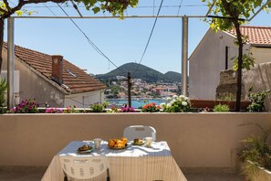 A balcony with a table set for breakfast, overlooking a coastal town and hills. - Apartment Meet & Greet (Dubrovnik)