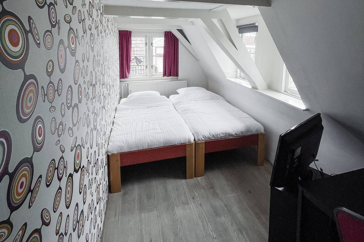 A bedroom with a sloped ceiling, a bed, a desk, and a chair.