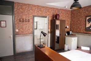 Une chambre d’hôtel avec un mur en briques, un bureau en bois, un miroir, une armoire, un petit réfrigérateur et un lit.