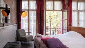 Una habitación con cama, una silla, un escritorio y ventanas amplias con cortinas.