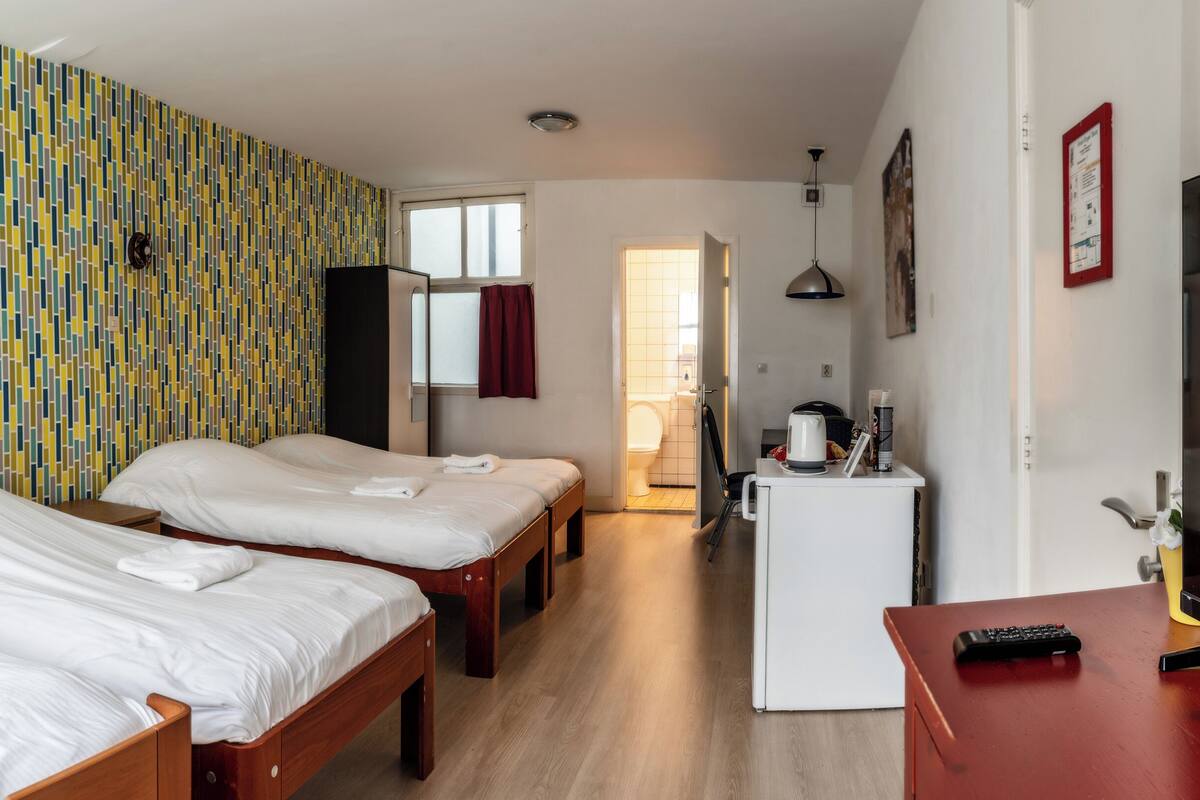 A hotel room with two single beds, a small kitchenette, a TV, and a patterned wall.