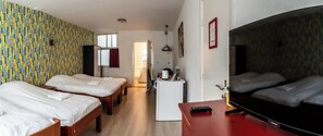 Une chambre d’hôtel avec deux lits simples, une petite kitchenette, une télévision et un mur décoré d’un motif.