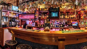 Un bar con una barra curva, varias botellas y una pantalla mostrando la carta.