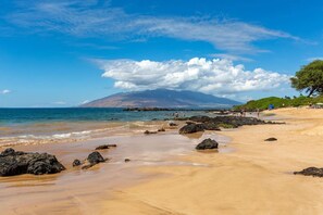 A beach with clear skies, a mountain in the background, and rocky outcrops. - Steps to the Beach w/ Ocean View - Kamaole Sands 5-304 (Kihei)