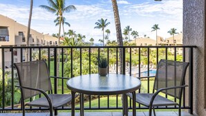 Un balcon avec deux chaises et une table, donnant sur une piscine et des palmiers.