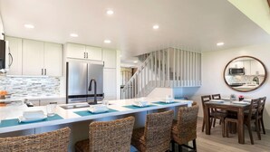 A modern kitchen with white cabinets, a stainless steel refrigerator, and a central island with bar stools. - Sweeping Views - Spacious 3 Bds! (Waikoloa Village)