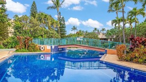 En klar, blå swimmingpool omgivet af frodig, tropisk vegetation og en turkis bro.