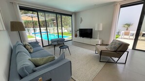 Un salon moderne avec un canapé, une table basse, un téléviseur et une vue sur une piscine.