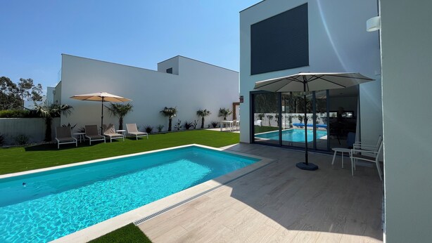 Un espace piscine extérieur moderne, doté d’une piscine à l’eau d’un bleu limpide, entourée d’une pelouse bien entretenue et de palmiers.