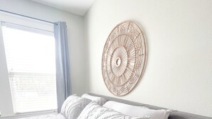 A neatly made bed with patterned bedding, a round wall hanging, and a window with curtains. - Kalmia Suite A - Centrally Located Downtown (Laurel)