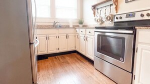 A kitchen with wooden flooring, white cabinets, a stainless steel refrigerator, and an oven. - Kalmia Suite A - Centrally Located Downtown (Laurel)
