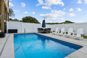 Relax by the pool surrounded by lush trees and a clear sky.