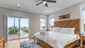 A bedroom with a large bed, a ceiling fan, and a view of the outdoors through sliding glass doors. - Never Lost in Emerald Isle, NC (Emerald Isle)
