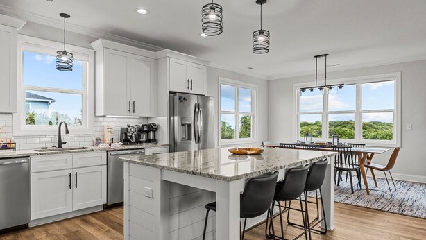 A modern kitchen with white cabinets, stainless steel appliances, and a large island with bar stools. - Never Lost in Emerald Isle, NC (Emerald Isle)