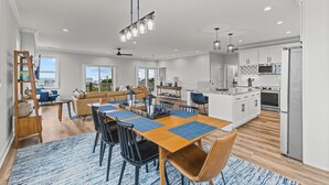 A spacious kitchen with white cabinets, a central island, and a dining area with a wooden table and chairs. - Never Lost in Emerald Isle, NC (Emerald Isle)