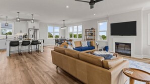 A spacious living area with a sofa, a dining table, and a kitchen area with a refrigerator and bar stools. - Never Lost in Emerald Isle, NC (Emerald Isle)
