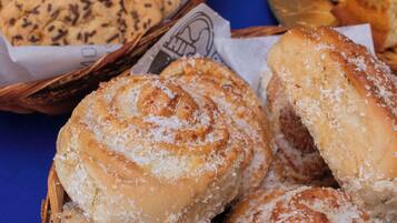 A basket of freshly baked pastries, including cinnamon rolls and bread, on a blue tablecloth.