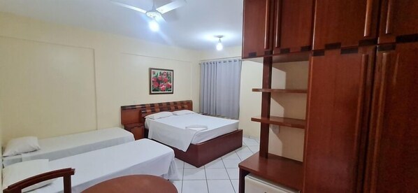 Una habitación de hotel con cama, escritorio, silla, armario y ventilador de techo.