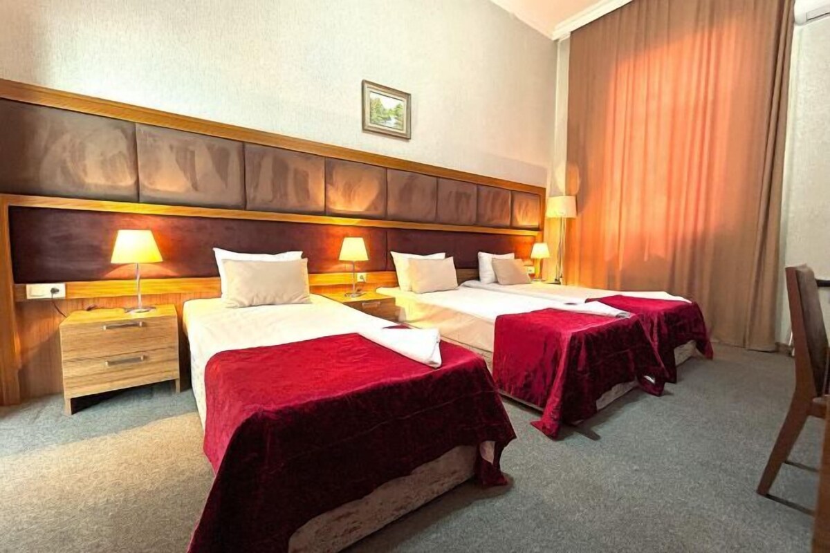 Habitación de hotel con dos camas, cada una con colcha roja, cabecero de madera y lámparas de noche.
