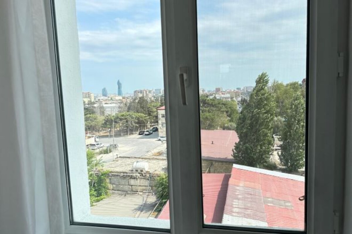 Vista desde una ventana sobre un paisaje urbano con edificios, árboles y cielo despejado.