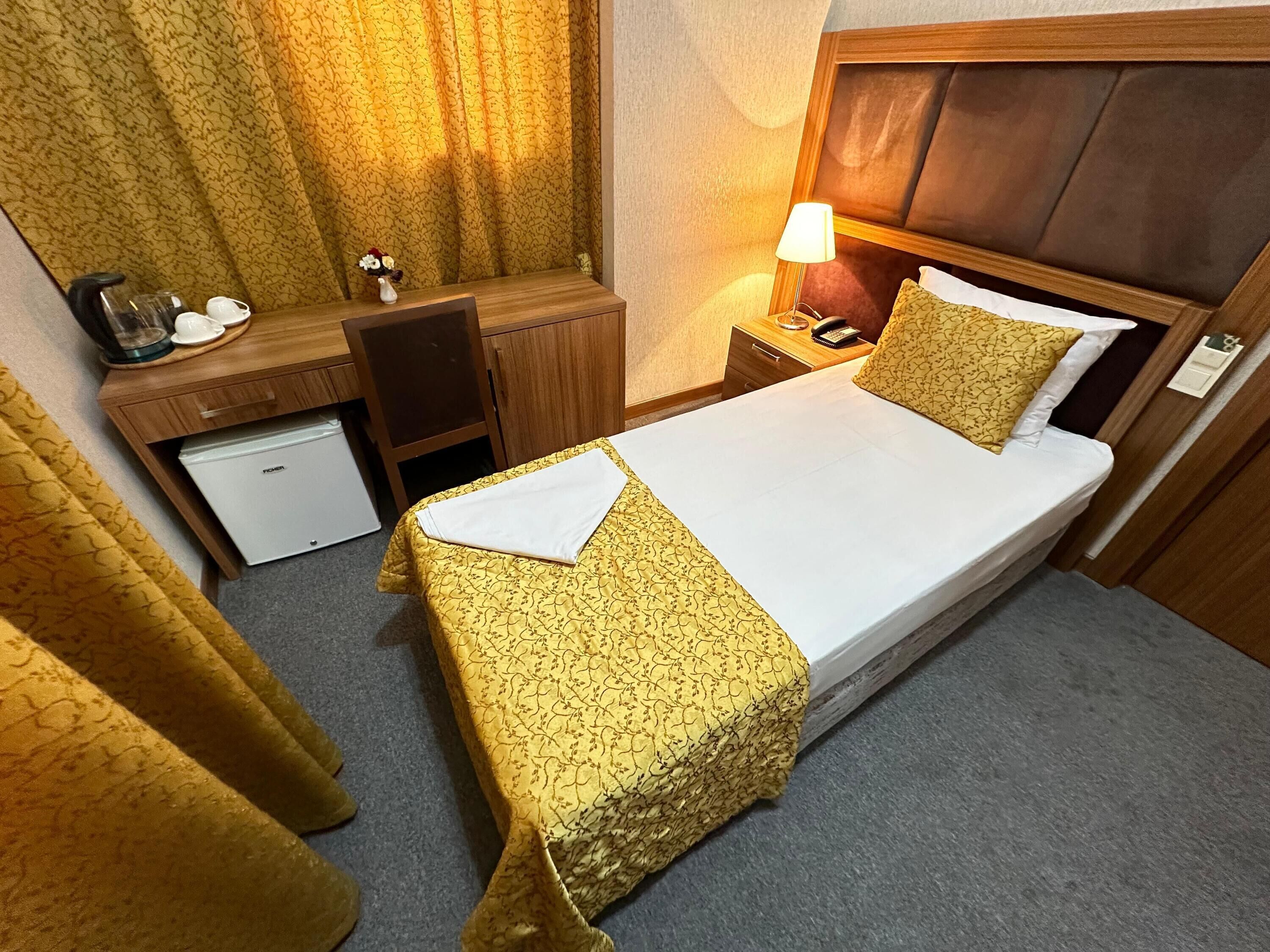 Quarto de hotel com cama, escrivaninha, cadeira, pequena geladeira, luminária e telefone.