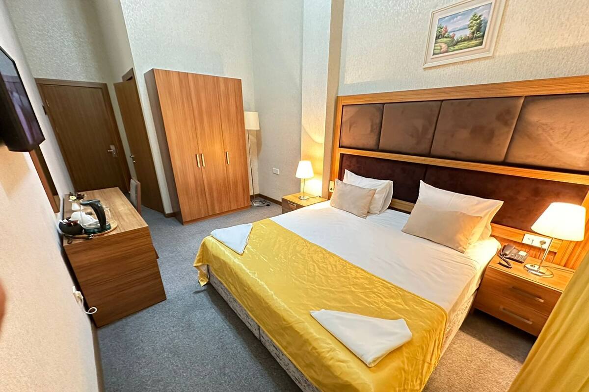 A hotel room with a bed, bedside tables, a wardrobe, and a painting on the wall.