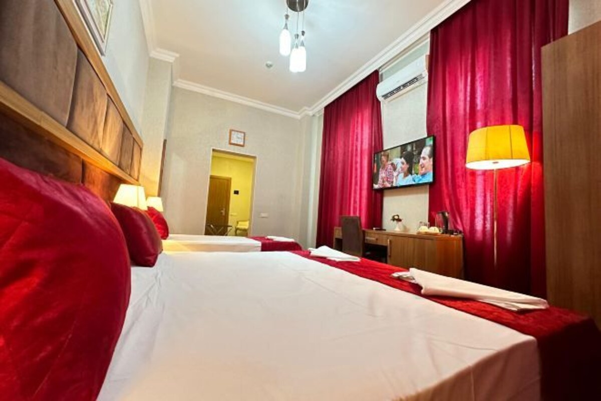 Een hotelkamer met twee bedden, rode gordijnen, een bureau, een stoel, een televisie en een lamp.