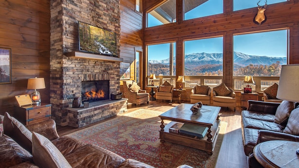 Una sala de estar acogedora con chimenea de piedra, muebles de cuero y grandes ventanales con vistas a la montaña.