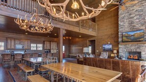 Un amplio salón con una gran mesa de comedor de madera, asientos cómodos, una chimenea y un balcón con barandillas de madera.