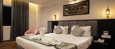 A hotel room with a large bed, a chair, a bedside table with a phone, and a painting on the wall.