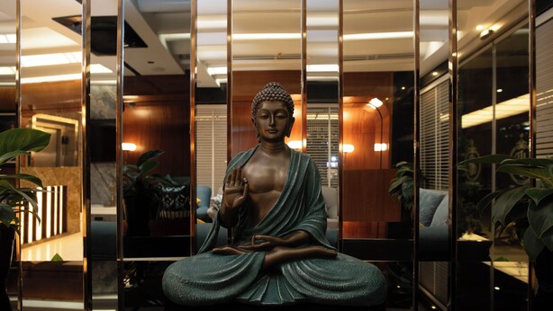 Een standbeeld van een zittende figuur in een kamer met een modern interieur, inclusief een bank en een potplant.