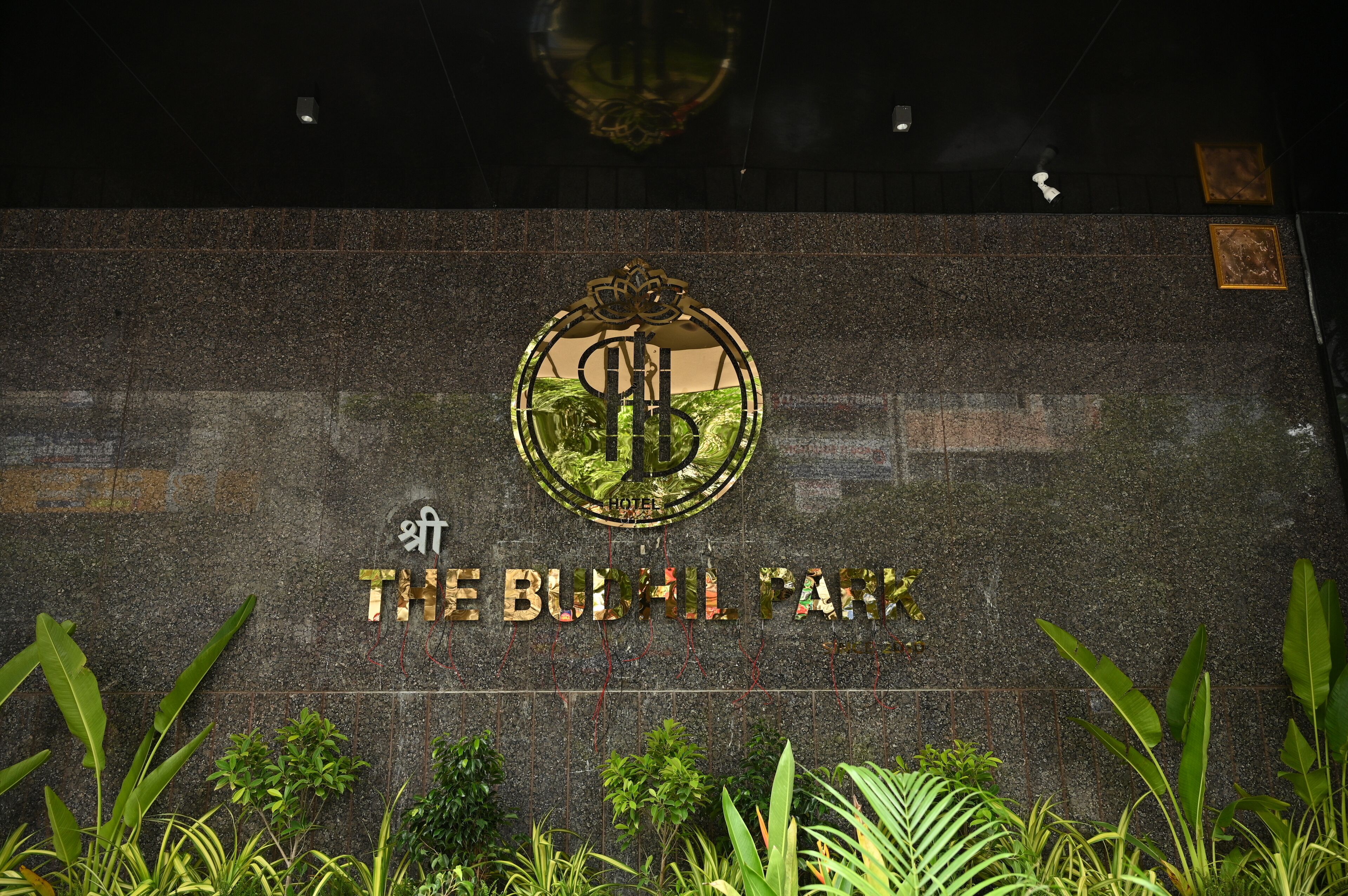 Un letrero del Hotel Budhill Park con un logo y el nombre en letras doradas sobre una pared de piedra.