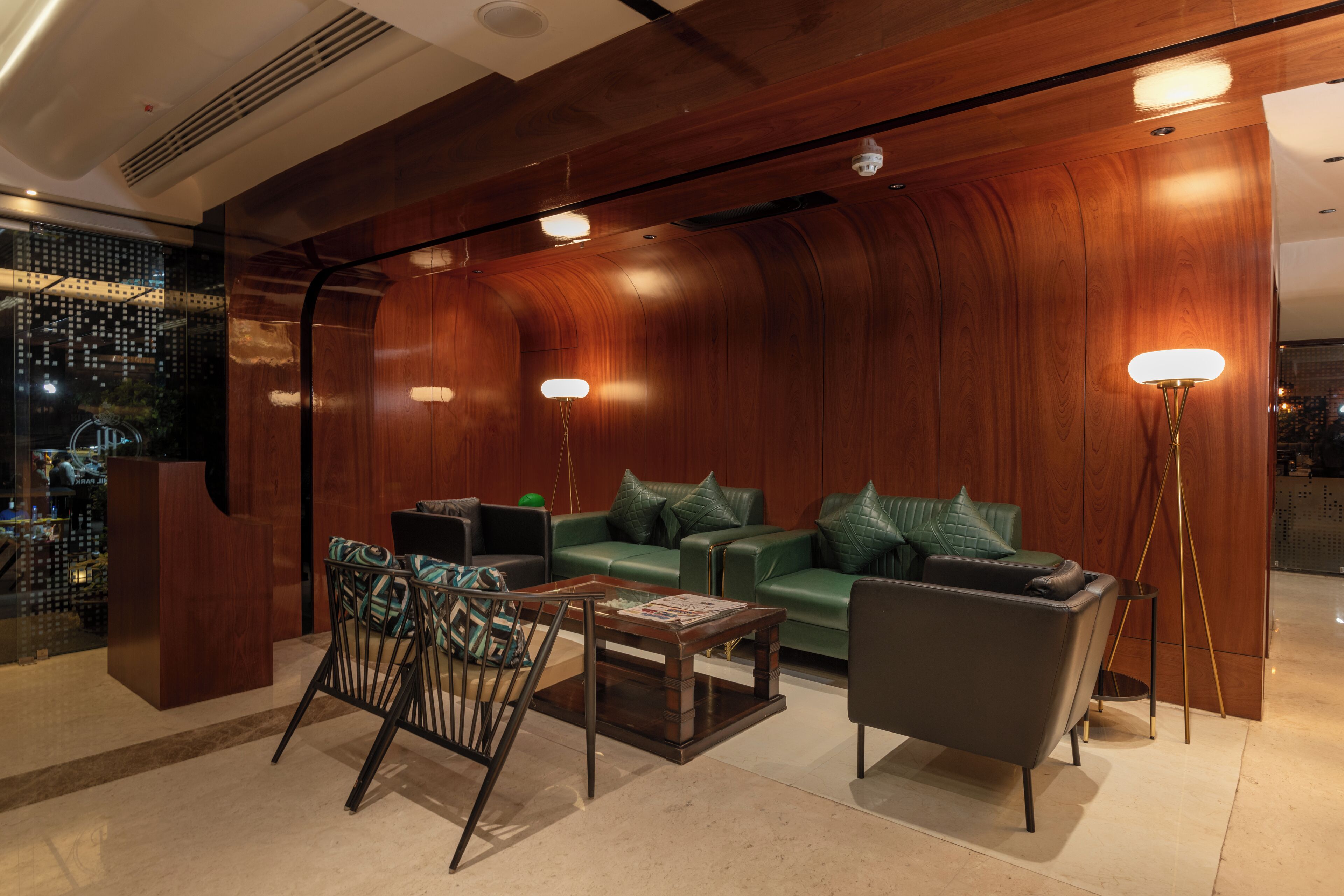 A modern lobby with a green leather sofa, a wooden reception desk, and a floor lamp.
