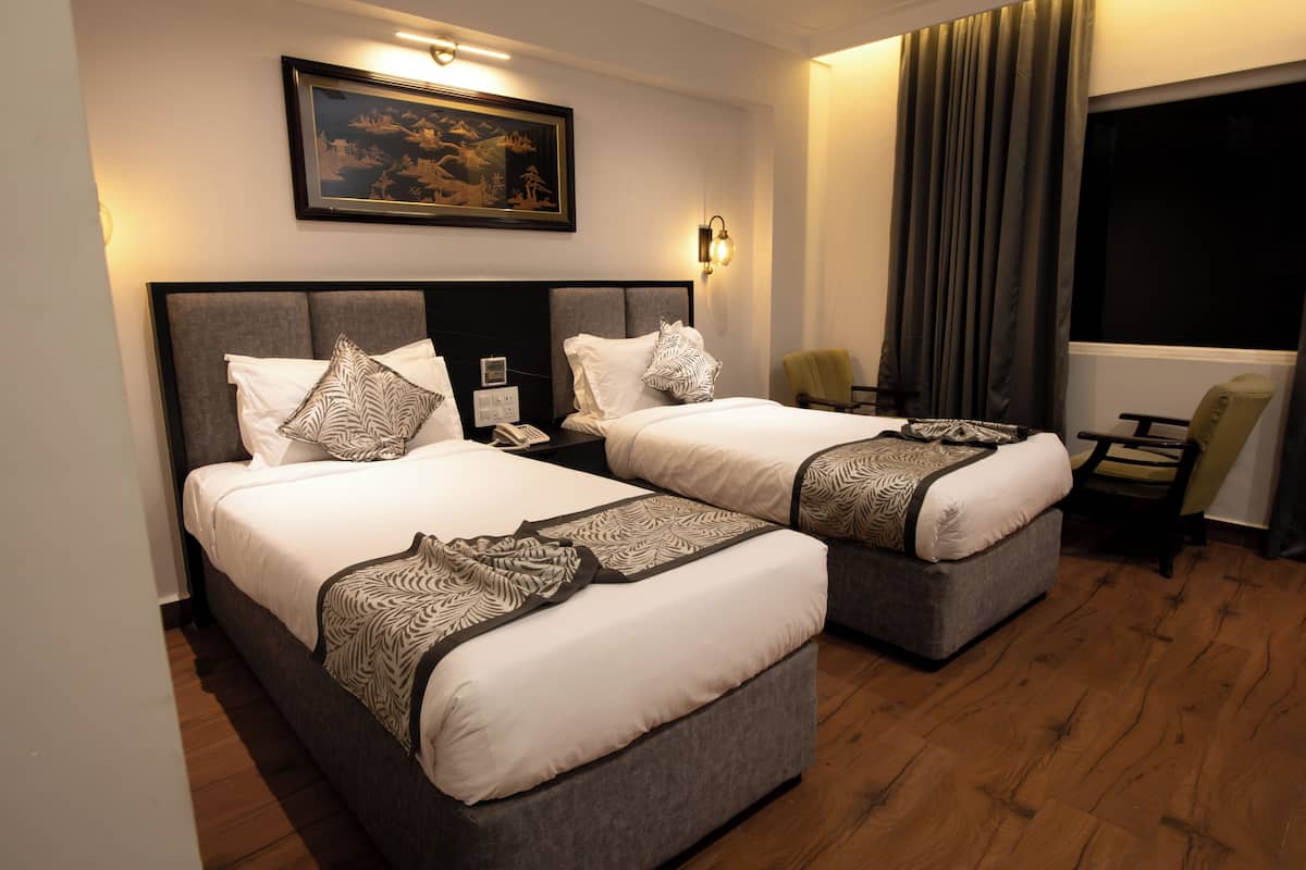 A hotel room with two beds, a nightstand, a chair, a window with curtains, and a framed picture on the wall.