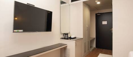 Una habitación de hotel moderna con un televisor de pantalla plana montado en la pared, una kitchenette pequeña con cafetera, y una puerta que da a otra habitación.