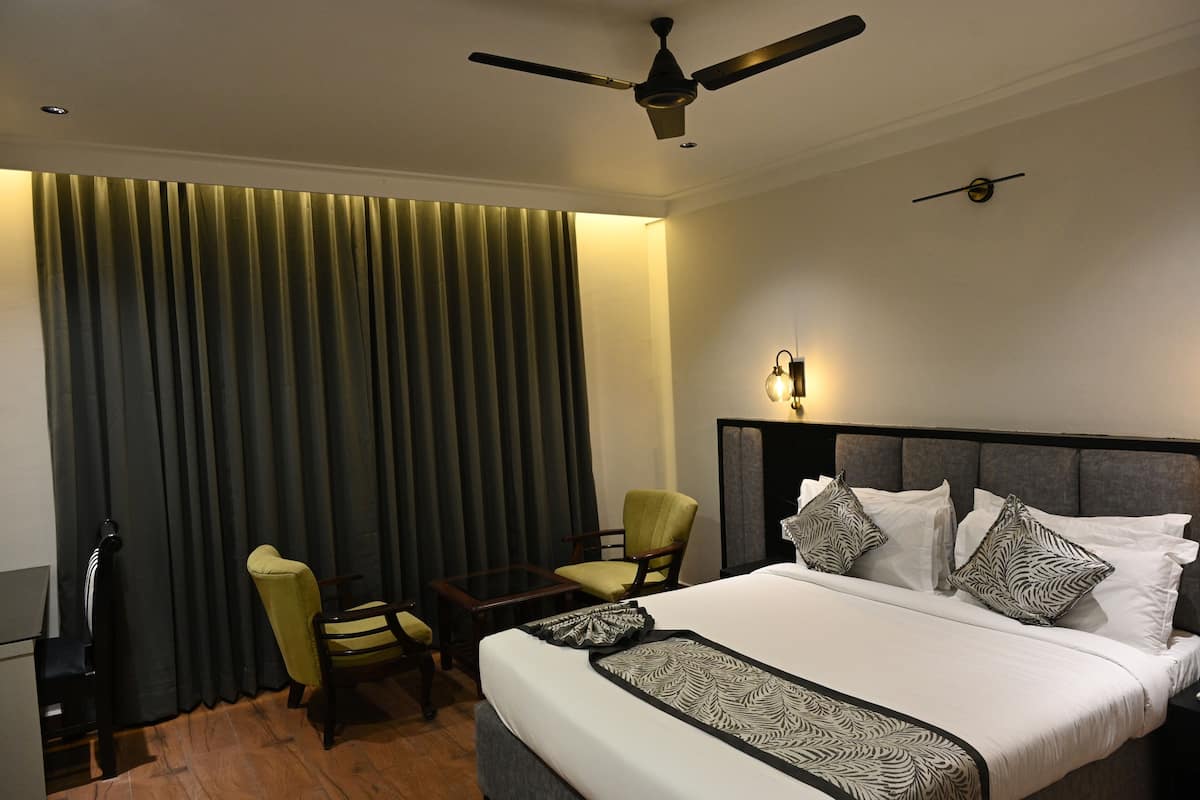 A hotel room with a large bed, two armchairs, a small table, a ceiling fan, and a wall-mounted light.