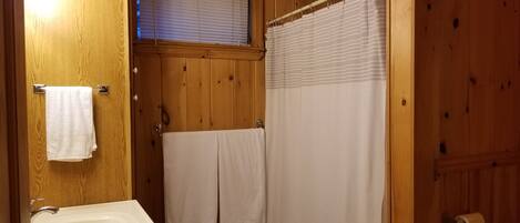 A wooden bathroom with a bathtub, two towels hanging on the wall, and a shower curtain.
