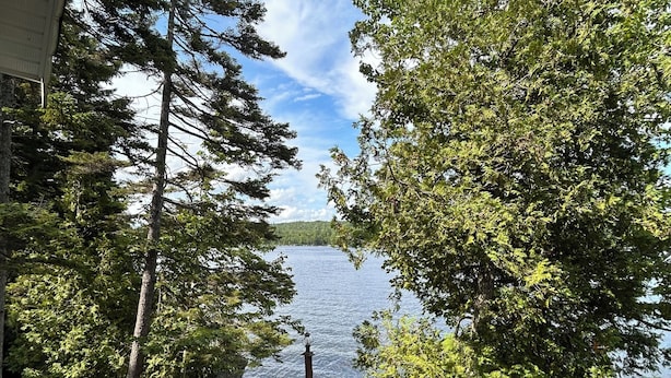 A wooden deck with a table and chairs overlooking a lake, surrounded by trees.