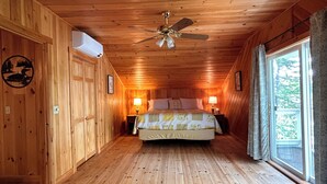 A wooden cabin bedroom with a bed, ceiling fan, and large window.