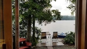 A wooden deck with two lounge chairs facing a calm lake, surrounded by trees.