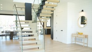 Un intérieur moderne avec un escalier en verre, un plancher en bois et un coin repas comprenant des tables et des chaises.