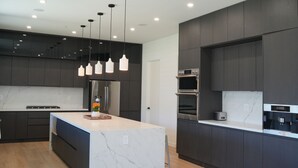 Une cuisine moderne avec des meubles de couleur sombre, un plan de travail en marbre et des luminaires suspendus.