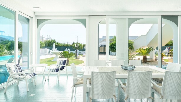 A spacious patio with white wicker furniture, a dining table, and a view of a swimming pool and greenery. - Villa Mar Mar con piscina by Wonderful Italy (Bari)