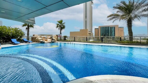 Une piscine à l’eau d’un bleu cristallin, entourée de palmiers et avec un bâtiment moderne en arrière-plan.