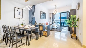 Un salon moderne avec un canapé, une table à manger pour quatre personnes et une grande fenêtre donnant sur l’extérieur.