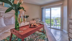 A spacious living room with a large window, a wooden coffee table with a floral rug, a sofa, and a balcony with a view. - Ocean Pointe Ocean View w/heated pool beach marina (Tavernier)