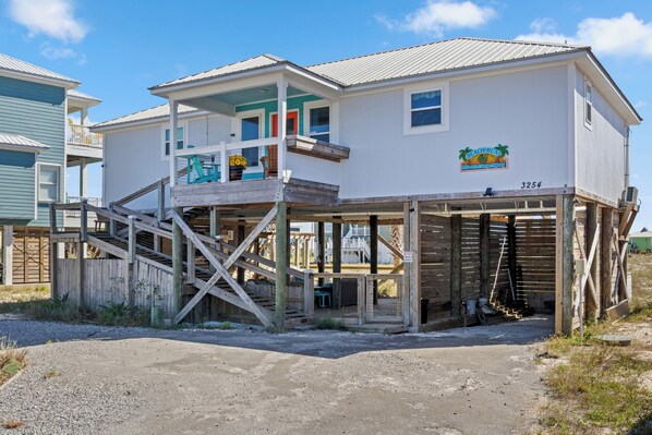 Ein zweistöckiges Haus mit Balkon, einer Holzterrasse und einem Schild, das es als Strandhaus kennzeichnet.