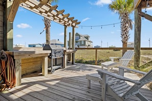 Eine Holzterrasse mit Grill, Stühlen und einer Pergola.