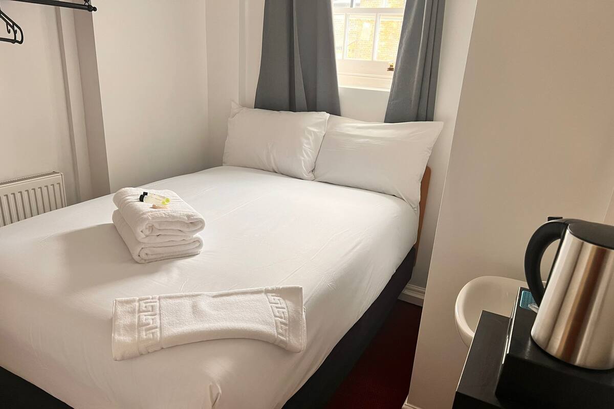 A neatly made bed with white linens, a folded towel, and a decorative towel on the bed.